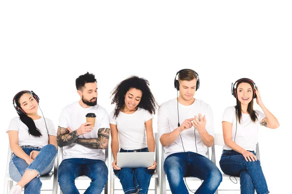 Multicultural group of young people using digital devices while man holding coffee to go isolated on white — Stock Photo