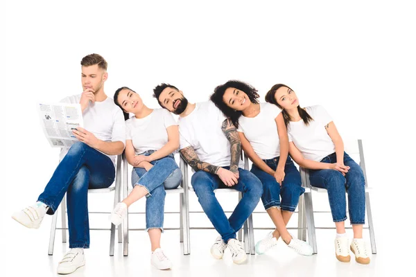 Multicultural group of young people lying on shoulders of each other while man reading newspaper isolated on white — Stock Photo