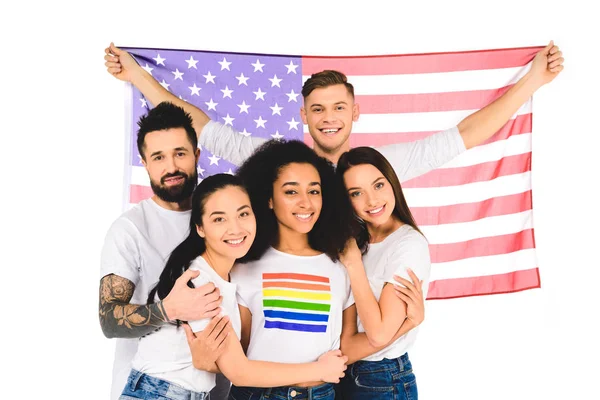 Grupo multiétnico de jóvenes que sonríen y se abrazan mientras sostienen la bandera de EE.UU. aislada en blanco - foto de stock