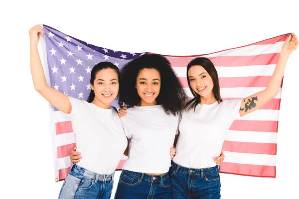 Multiethnic group of girls smiling and hugging while holding flag of usa isolated on white — Stock Photo