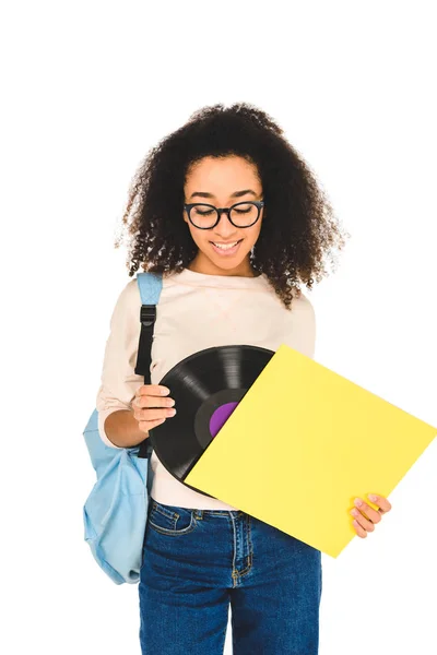 Chica afroamericana de pie en gafas y mirando disco de vinilo aislado en blanco - foto de stock