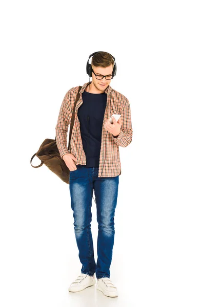 Bell'uomo in piedi in cuffia e utilizzando smartphone isolato su bianco — Foto stock