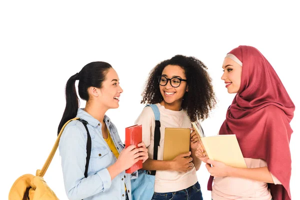 Alegre multicultural niñas de pie y riendo con libros aislados en blanco - foto de stock