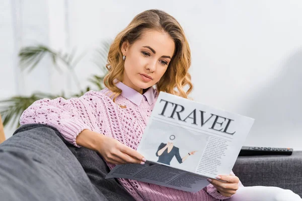 Mulher atraente sentado no sofá e ler jornal de viagem na sala de estar — Fotografia de Stock