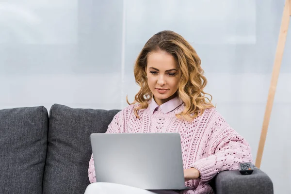 Hübsche Frau sitzt auf Sofa und schaut auf Laptop-Bildschirm im Wohnzimmer — Stockfoto