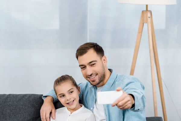 Щасливий батько і дочка сидять на дивані і приймають селфі в квартирі — стокове фото