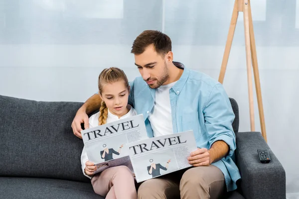 Father and daughter sitting on sofa and reading travel newspapers in living room — Stock Photo