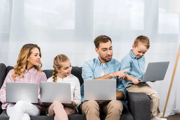 Famille assis sur le canapé et utilisant des ordinateurs portables ensemble — Photo de stock