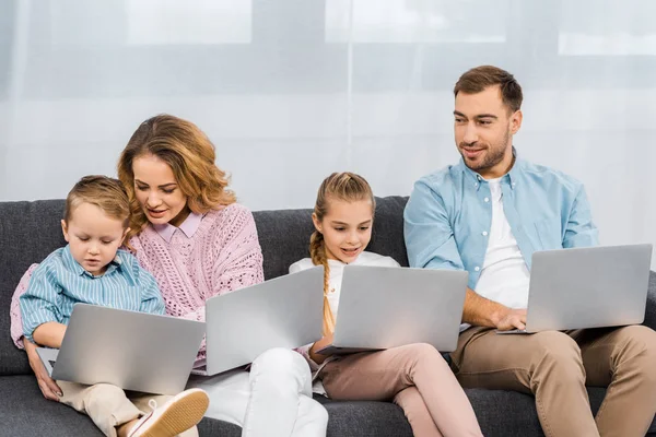 Familia feliz sentado en el sofá y el uso de computadoras portátiles en el apartamento - foto de stock