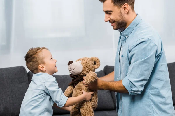 Souriant père et fils tenant ours en peluche dans le salon — Photo de stock