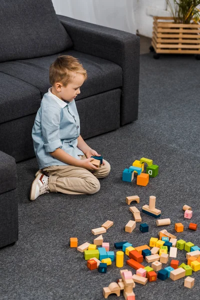 Niedliche Vorschulkind mit bunten Holzklötzen sitzt auf dem Boden im Wohnzimmer — Stockfoto