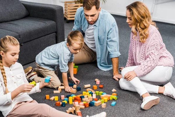 Parents and siblings playing with wooden blocks on floor in living room — Stock Photo