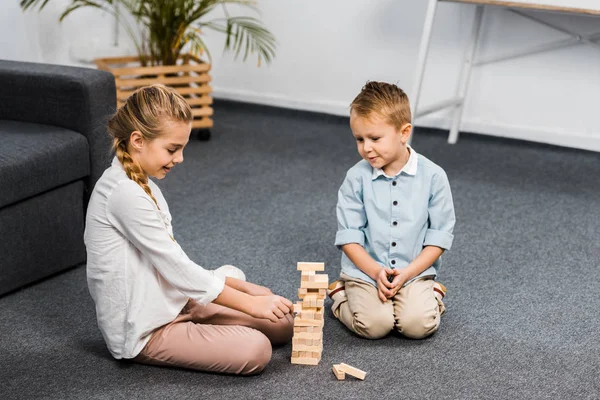 Frères et sœurs mignons assis sur le sol et les blocs de jeu tour en bois jeu dans le salon — Photo de stock