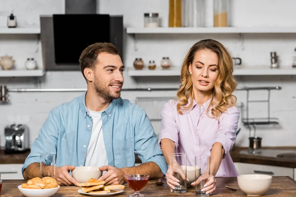 Homme souriant regardant jolie femme mettant des lunettes sur la table de cuisine — Photo de stock