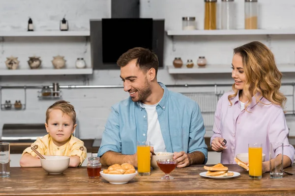 Smiling parents looking at cute boy sitting at kitchen table — Stock Photo