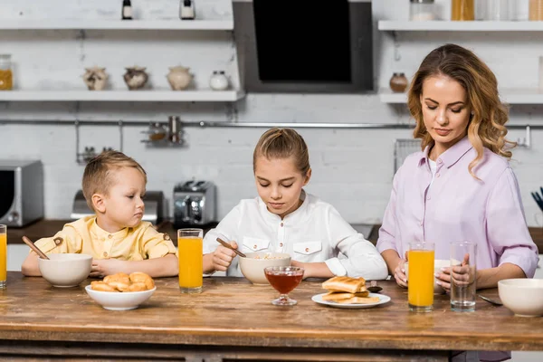 Cute siblings with mom eating porridge at table — Stock Photo