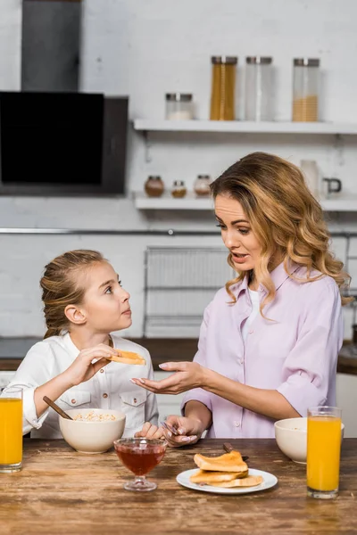 Pretty mother giving toast to cute daughter at table — Stock Photo