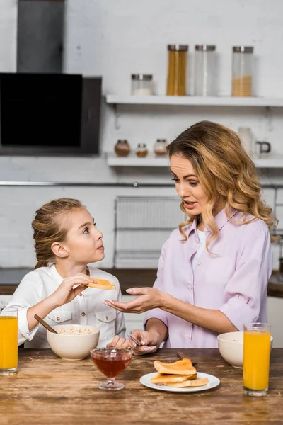 Jolie mère donnant toast à jolie fille à la table — Photo de stock