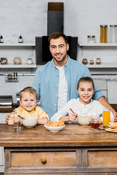 Souriant père avec frères et sœurs regardant caméra à la table de cuisine — Photo de stock