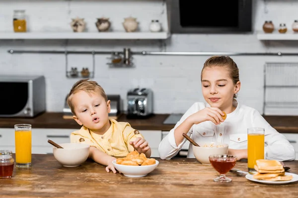 Cute siblings sitting at table and holding cookies — Stock Photo