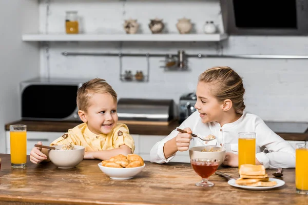 Lächelnde Geschwister essen Brei am Tisch und schauen einander an — Stockfoto