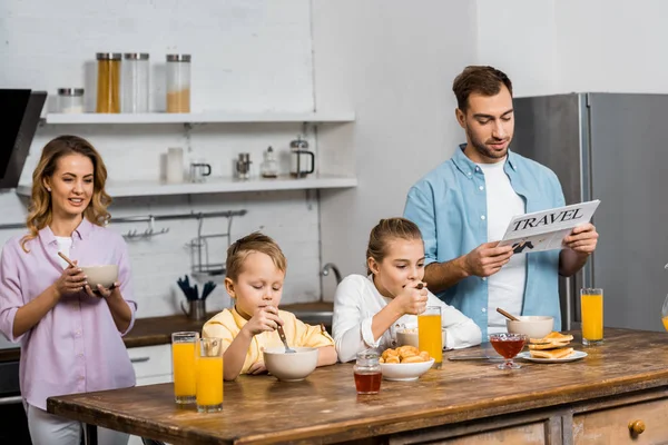 Sohn und Tochter essen Haferflocken, während Vater in der Küche Reisezeitung liest — Stockfoto