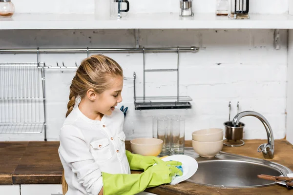 Linda chica en guantes de goma lavar los platos en la cocina - foto de stock