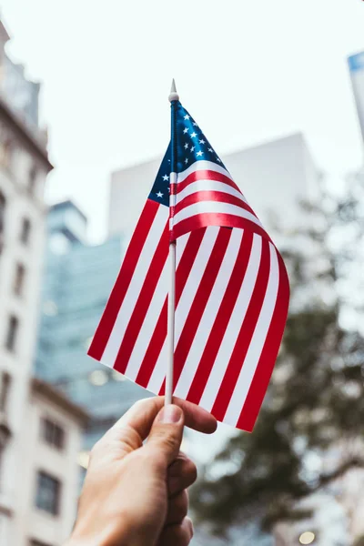 Cortado tiro de homem segurando bandeira americana na mão com desfocado nova york cidade rua no fundo — Fotografia de Stock