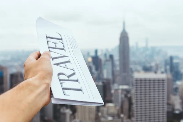 Vista parcial del hombre sosteniendo periódico de viaje con borrosa vista de la ciudad de Nueva York en el fondo - foto de stock
