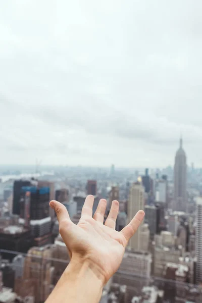 Vista parcial de la mano masculina y borrosa vista de la ciudad de Nueva York en el fondo - foto de stock
