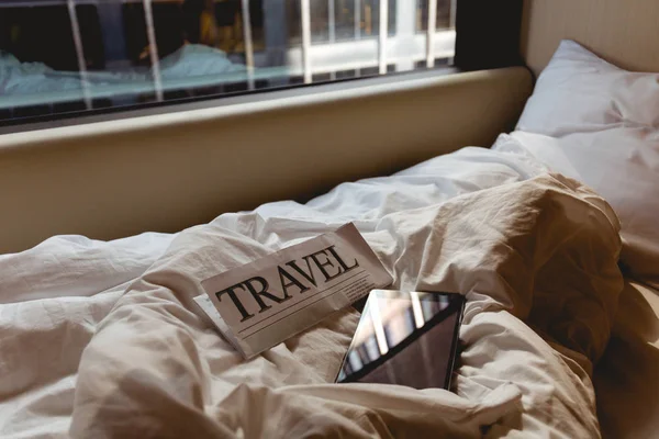 Vista de cerca del periódico de viaje y la tableta en la cama en la habitación del hotel - foto de stock