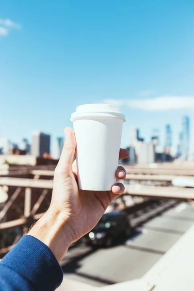 Partial view of man holding disposable cup of coffee with blurred new york city on background — Stock Photo