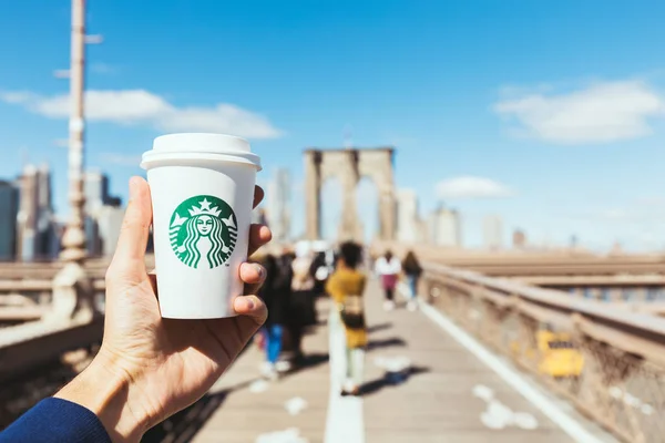NUEVA YORK, EE.UU. - 8 de octubre de 2018: vista parcial del hombre sosteniendo una taza de café desechable starbucks en el puente Brooklyn, Nueva York, EE.UU. - foto de stock