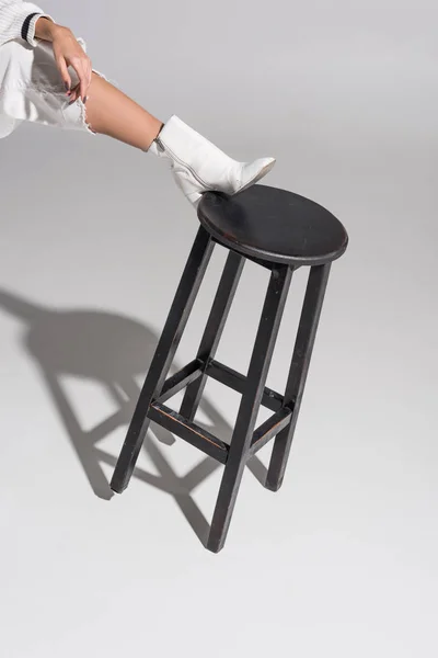 Cropped image of girl in stylish white shoe putting leg on black chair on white — Stock Photo