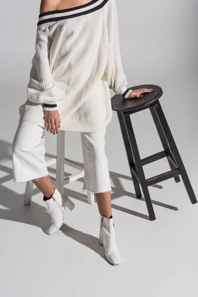 Cropped image of girl in fashionable white sweater and trousers sitting on white chair on white — Stock Photo