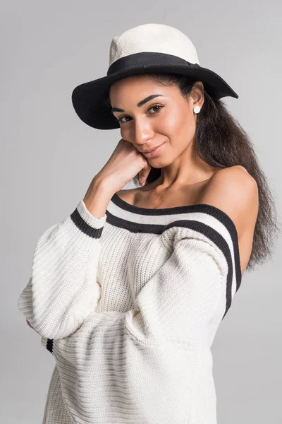 Atractiva chica americana africana alegre en suéter blanco con estilo y sombrero mirando a la cámara aislada en blanco - foto de stock