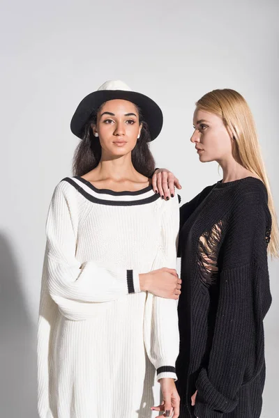 Hermosas mujeres afroamericanas y caucásicas en ropa blanca y negra de pie sobre blanco - foto de stock