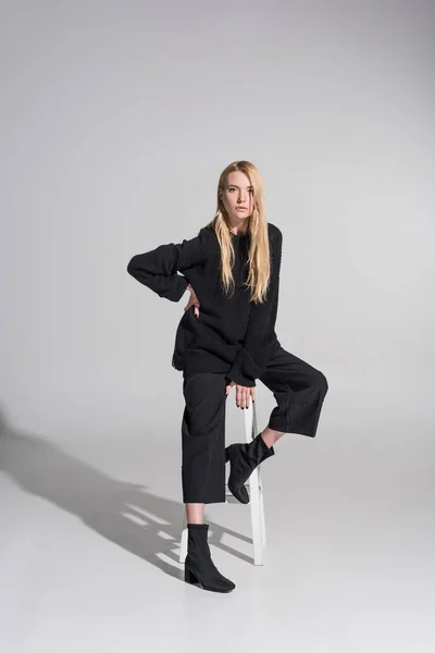 Beautiful caucasian blonde woman in black clothes sitting on chair and looking at camera on white — Stock Photo