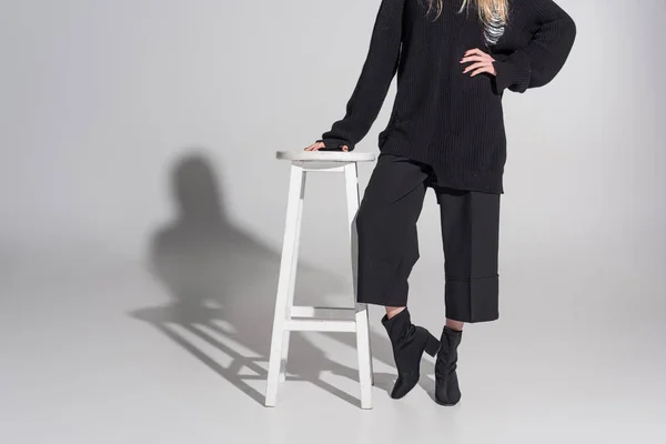 Cropped image of caucasian blonde woman in black clothes leaning on chair on white — Stock Photo