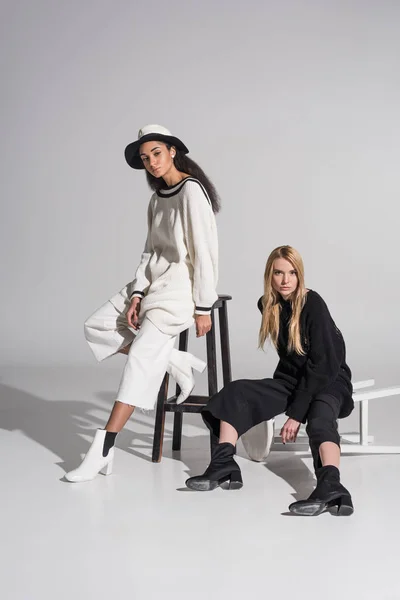 Beautiful multicultural women in stylish black and white clothes sitting on chairs on white — Stock Photo