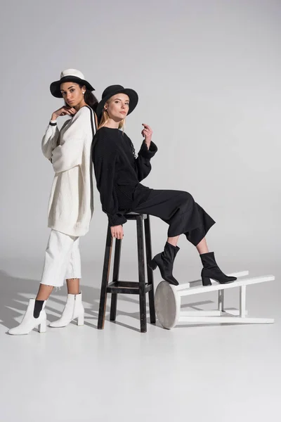 Attraktive multiethnische Frauen in schwarz-weißer Kleidung posieren mit Stühlen auf weißem Grund — Stockfoto