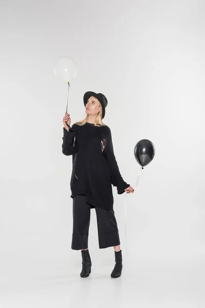 Beautiful caucasian blonde woman in black clothes and hat holding balloons on white — Stock Photo