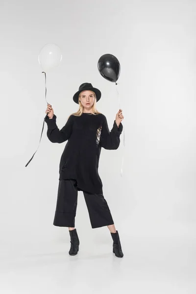 Beautiful caucasian blonde woman in black clothes and hat holding balloons and looking at camera on white — Stock Photo
