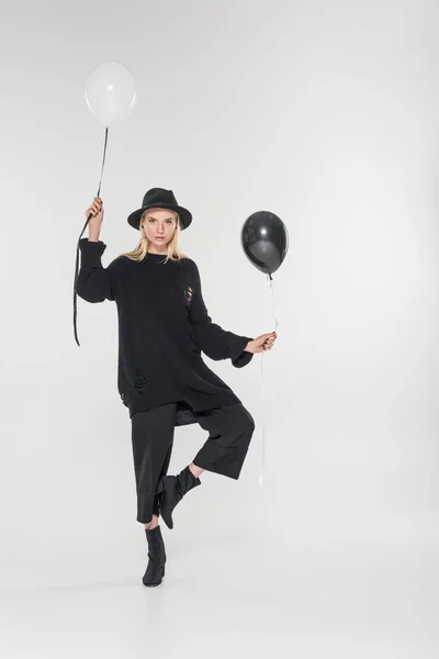 Hermosa mujer rubia caucásica en ropa negra y sombrero posando con dos globos en blanco - foto de stock