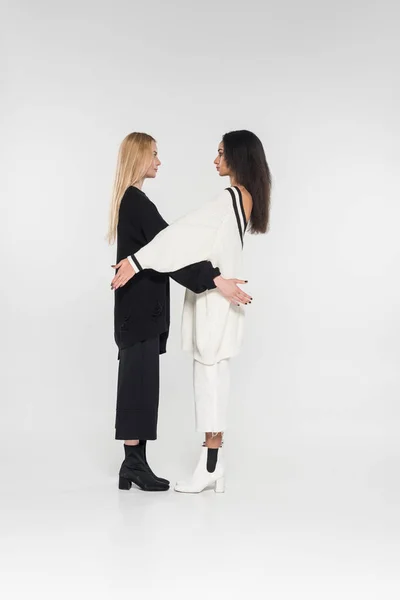 Schöne multikulturelle Frauen in schwarz-weißer Kleidung stehen und schauen einander auf weißem Grund an — Stockfoto