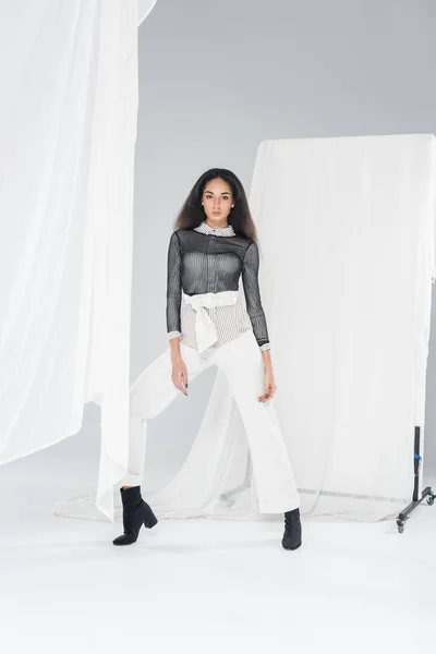 Attractive african american girl in stylish clothes posing near tulle on white — Stock Photo