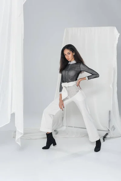 Beautiful african american girl in stylish clothes posing near tulle on white — Stock Photo