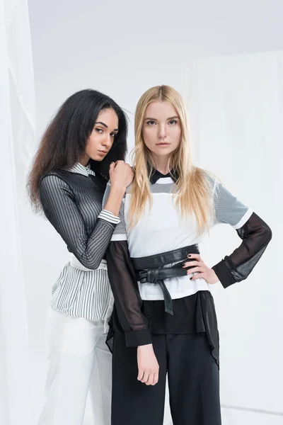 Attractive multicultural brunette and blonde women in black and white clothes posing isolated on white — Stock Photo