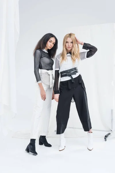 Longitud completa de hermosas mujeres multiculturales en ropa blanca y negra posando en blanco - foto de stock