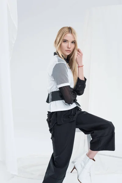 Seitenansicht der schönen kaukasischen Blondine in modischer schwarzer Kleidung sitzt auf Stuhl isoliert auf weiß — Stockfoto